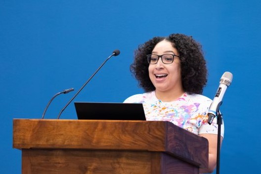 Student standing at a podium with a microphone and laptop, giving a speech.