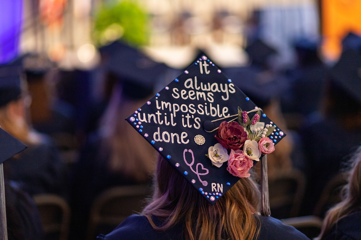 Graduate ceremony with graduate cap reading "it always seems impossible until it's done - RN".
