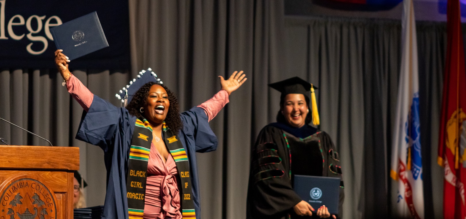 Graduate raises her hands to the sky, wearing a huge smile, as she crosses the stage during commencement ceremony.