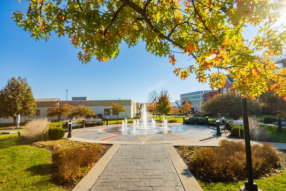 Distant view of Alumni fountain in full motion with main campus buildings in the background.