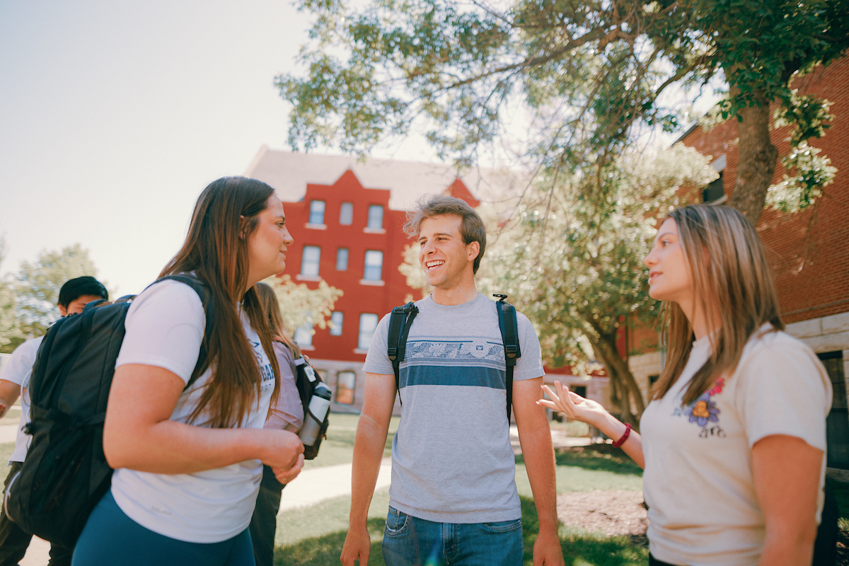 Three students standing outside on main campus, engaged in conversation.