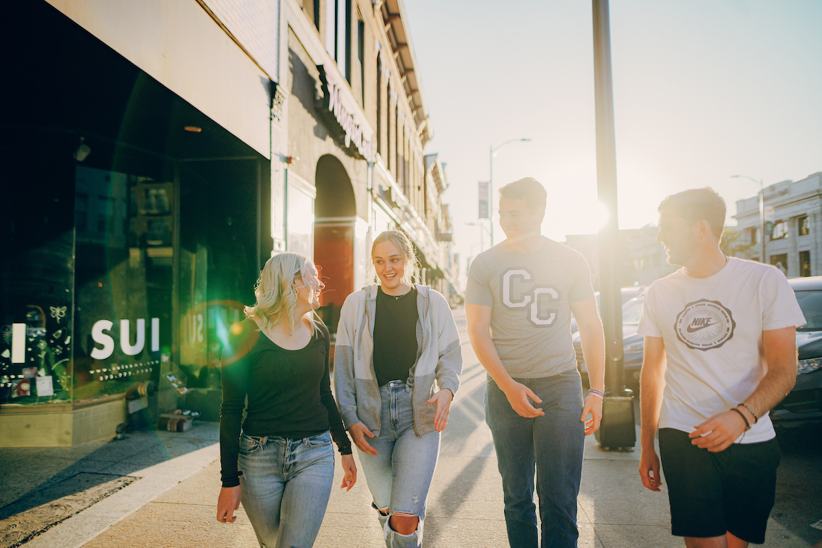 Group of students, one wearing a "CC" t-shirt, walking past the shops in downtown Columbia, MO.