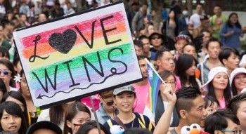 A group of gatherers holding a large colorful sign that says "Love Wins".