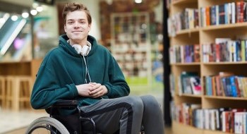 A young Caucasian male sitting on a wheelchair smiling at the camera
