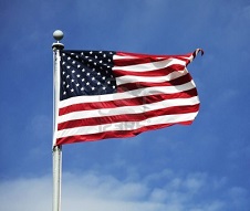 The American flag waving in the wind against a blue sky background.
