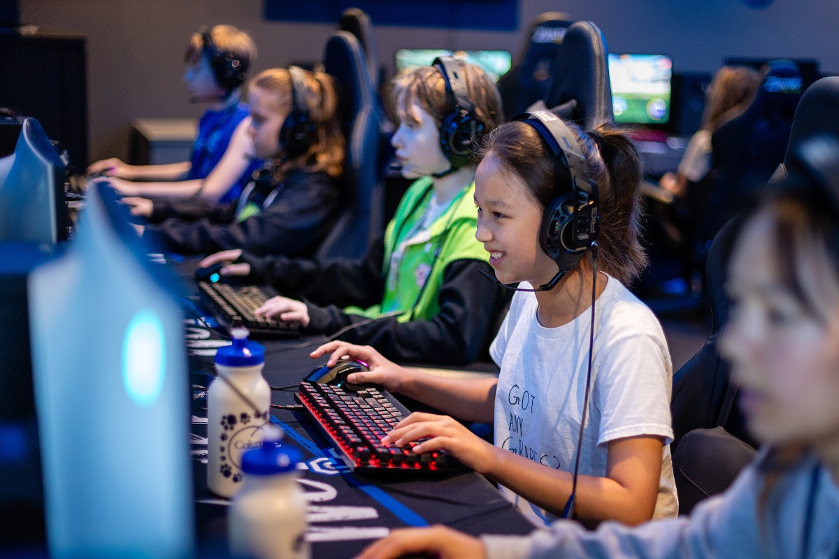 Group of campers playing on computers wearing headsets and using the mouse and keyboard.