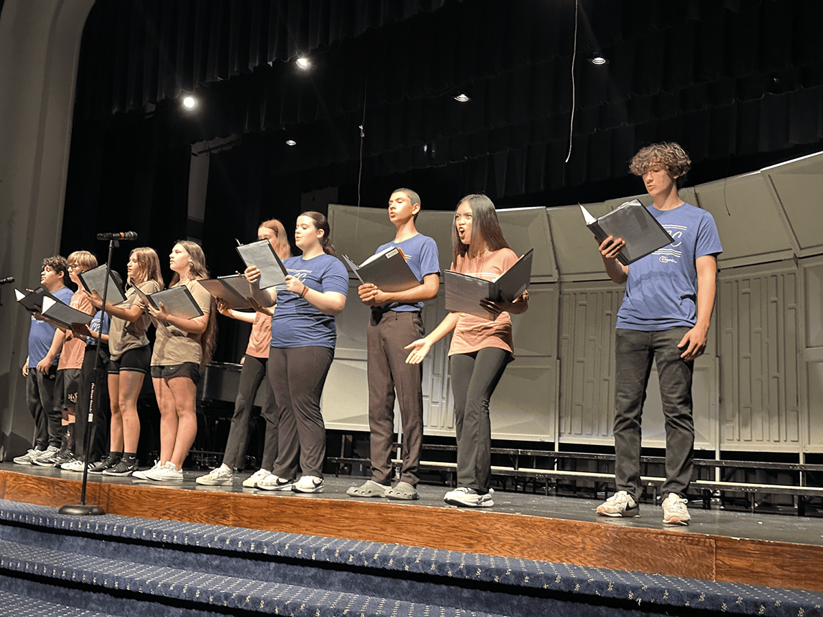 Ten campers lined up on stage performing a number, holding sheet music, and singing.