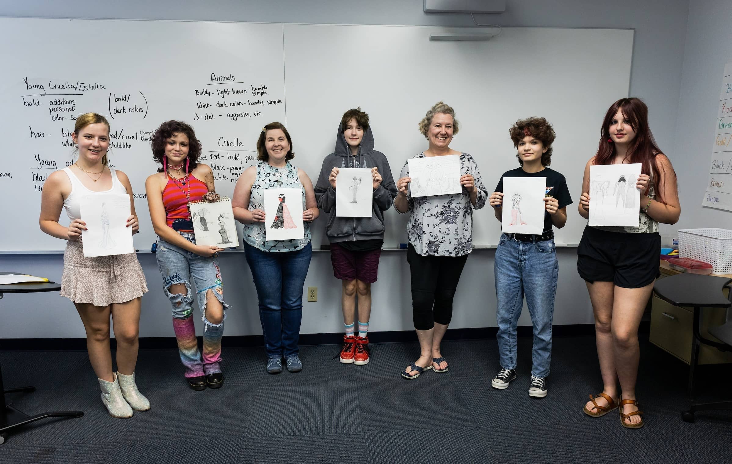Group of 7 camp members facing the camera, smiling proudly while holding their costume drawings.