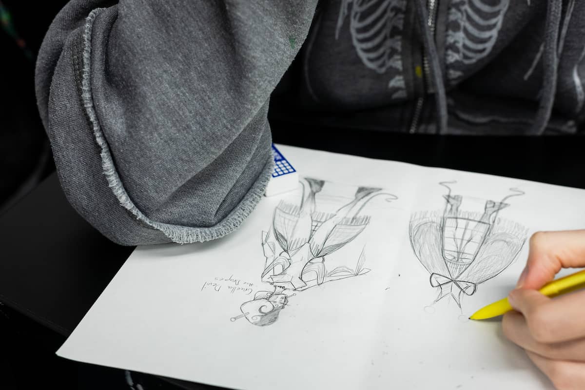 Camper sitting with a canvas, drawing characters in costume in pencil.