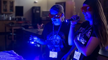 Two female campers using a black light to review staged crime scene evidence.