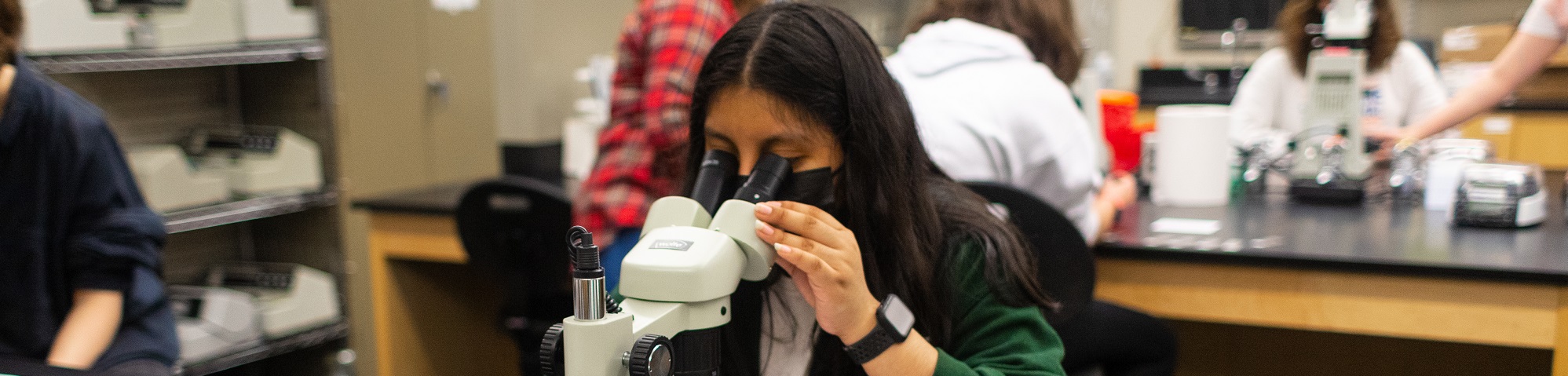 Female camper using a microscope to identify clues in the CSI: Columbia College summer camp.