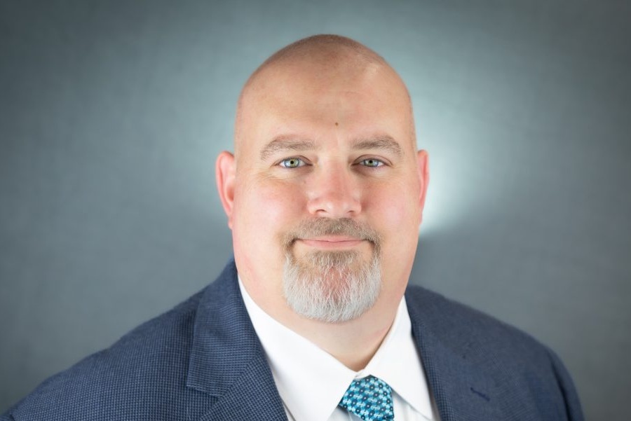 Headshot of Dave Hickman, wearing a dark suit, white shirt and patterned tie, smiling at the camera.