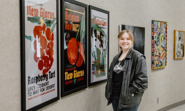 Profile image of Columbia College alumni, Isabella Dablemont, wearing a black leather jacket and standing in front of several pieces of hanging art.
