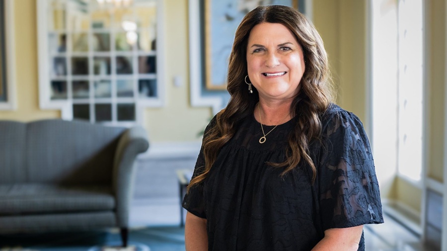 Dr. Rebekah Freese, wearing a short-sleeved dark shirt, pendant necklace and hoop earring, facing the camera and smiling.