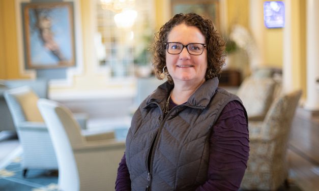 Dr. Shari Lawson, wearing a purple long sleeve shirt and gray vest, stands with arms crossed, smiling at the camera.
