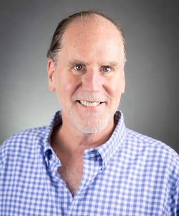 Dean David Karr, wearing a blue and white button-down shirt, smiling at the camera.