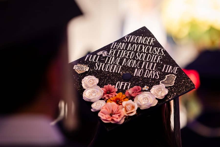 Commencement ceremony with mortarboard reading "Stronger than my excuses, retired soldier, full-time mom, full-time student, no days off!".