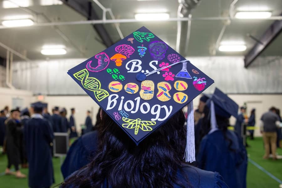 Commencement ceremony with mortarboard reading "B.S. Biology", surrounded by biology graphics.