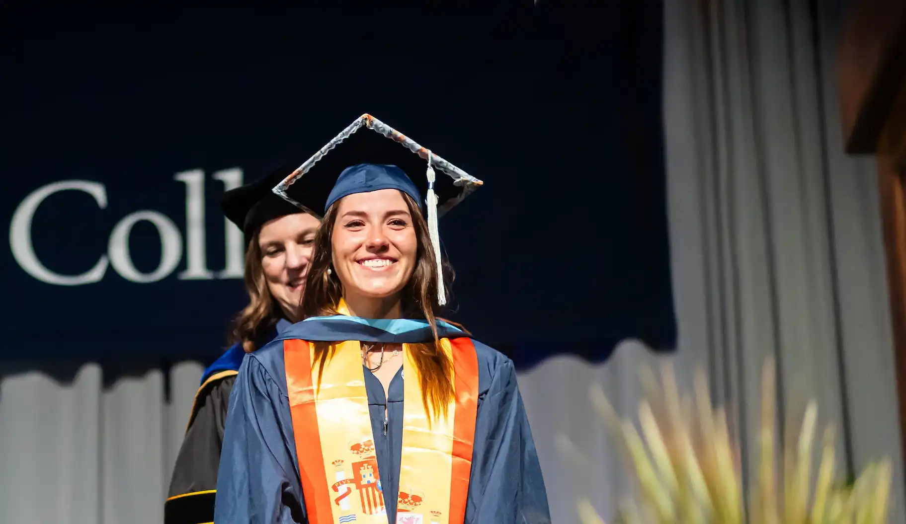 Columbia College graduate in full regalia smiling and looking out from the commencement stage as she is recognized for earning her degree.
