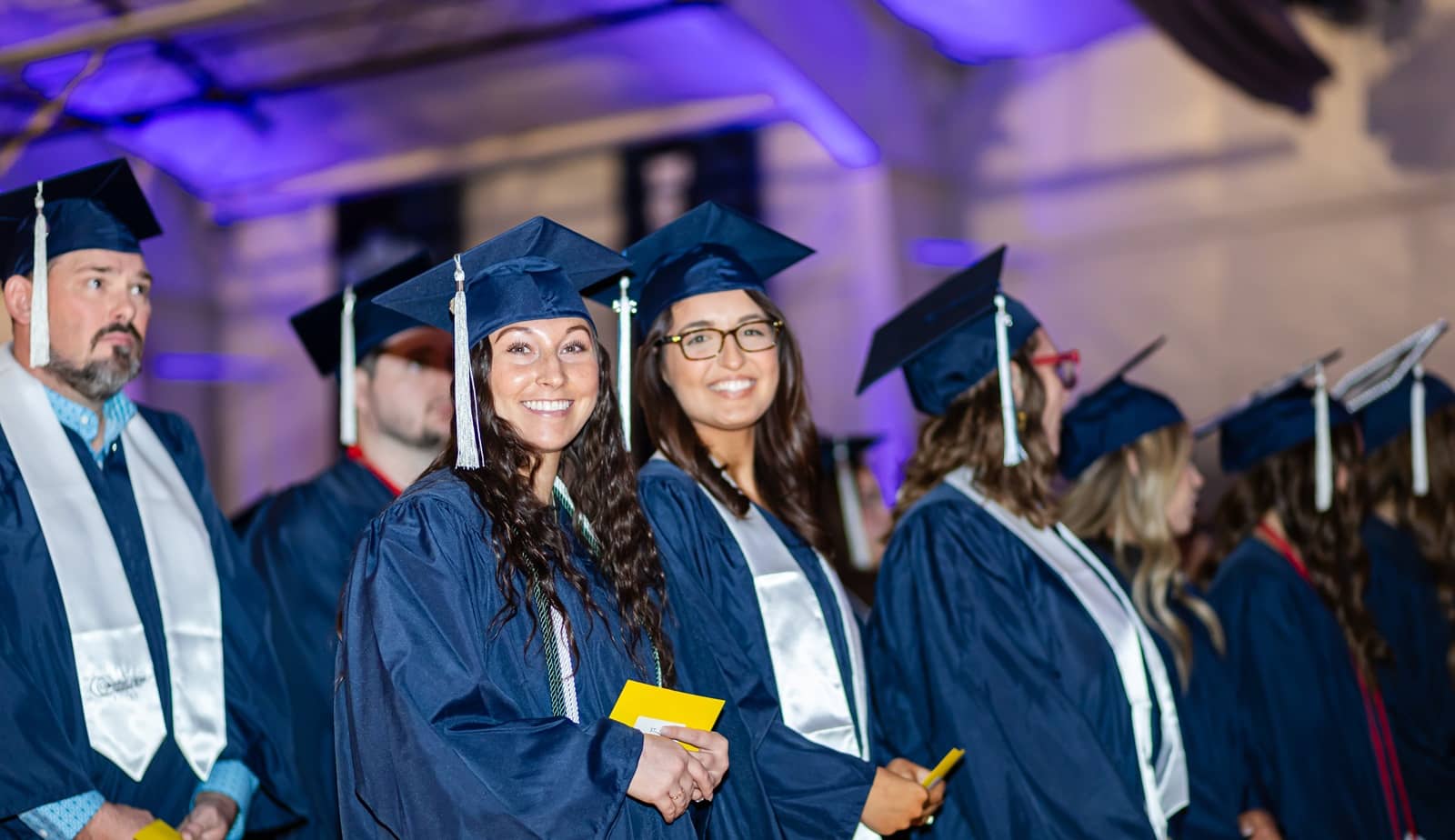Two Columbia College graduates smiling while surrounded by other graduates at commencement.