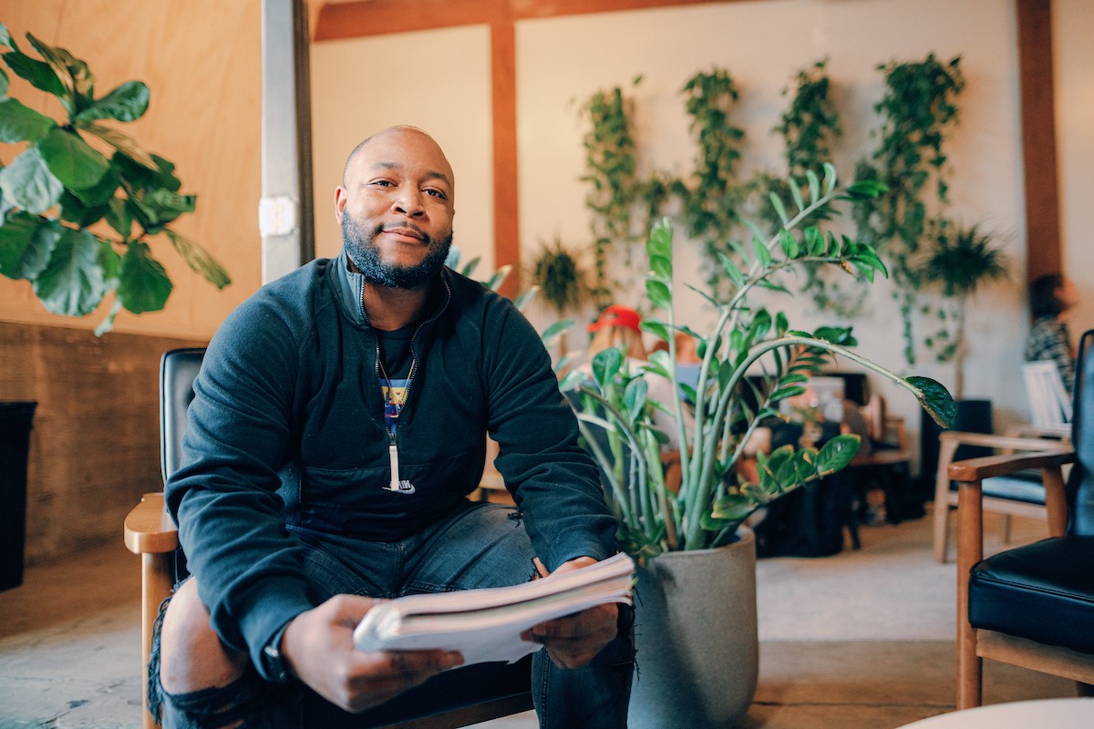 Graduate student sitting in a chair, holding a notebook and smiling at the camera.