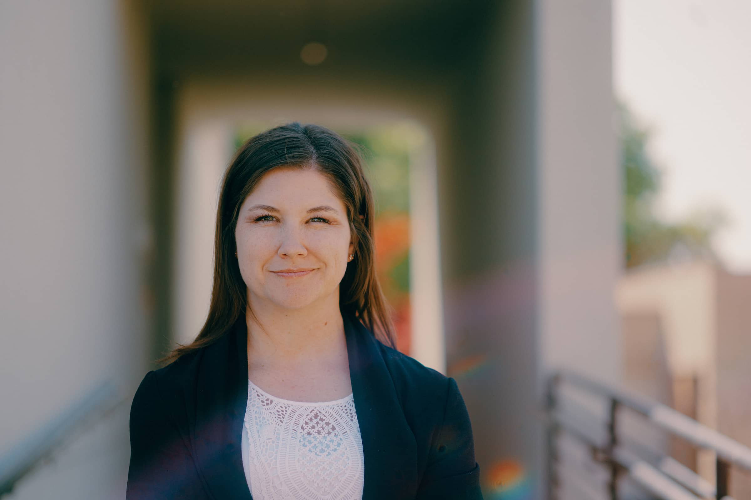 Female MS-MIS adult student, wearing a white top and dark blazer, standing outside and smiling at the camera.