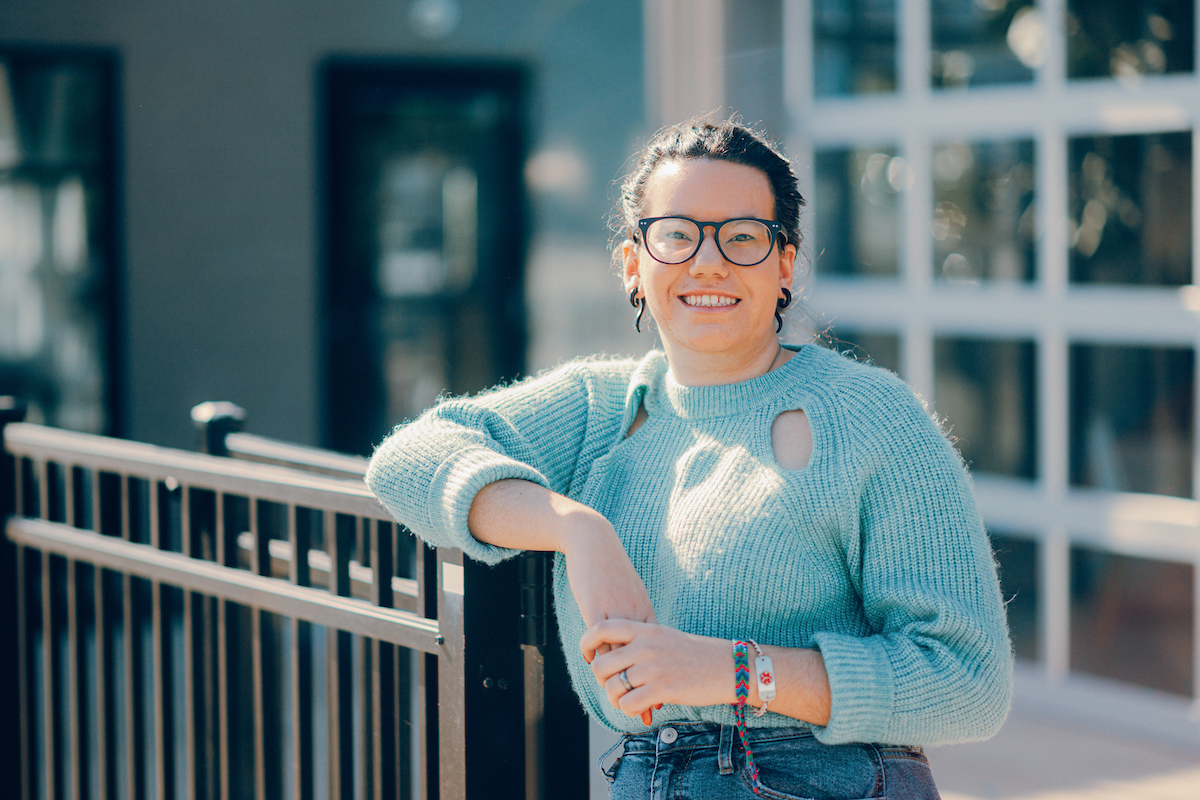 For Education Programs: Woman wearing glasses and smiling at the camera while leaning on a fence.