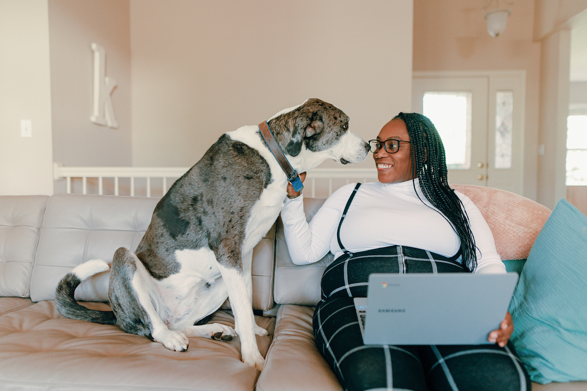 Women sitting on her couch with laptop while petting dog.