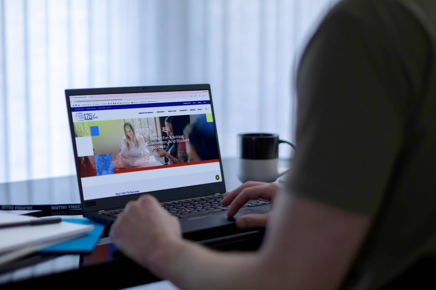 Student sitting at a table in front of a computer reviewing Columbia College's Center for Advising, Retention, and Student Success web page.