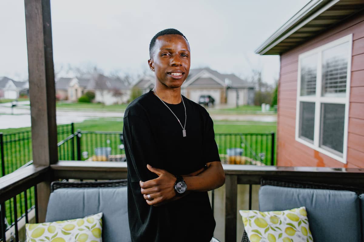Robert W. Plaster School of Business: Man wearing wearing a black t-shirt and pendant around his neck, with arms crossed standing outside on a deck.