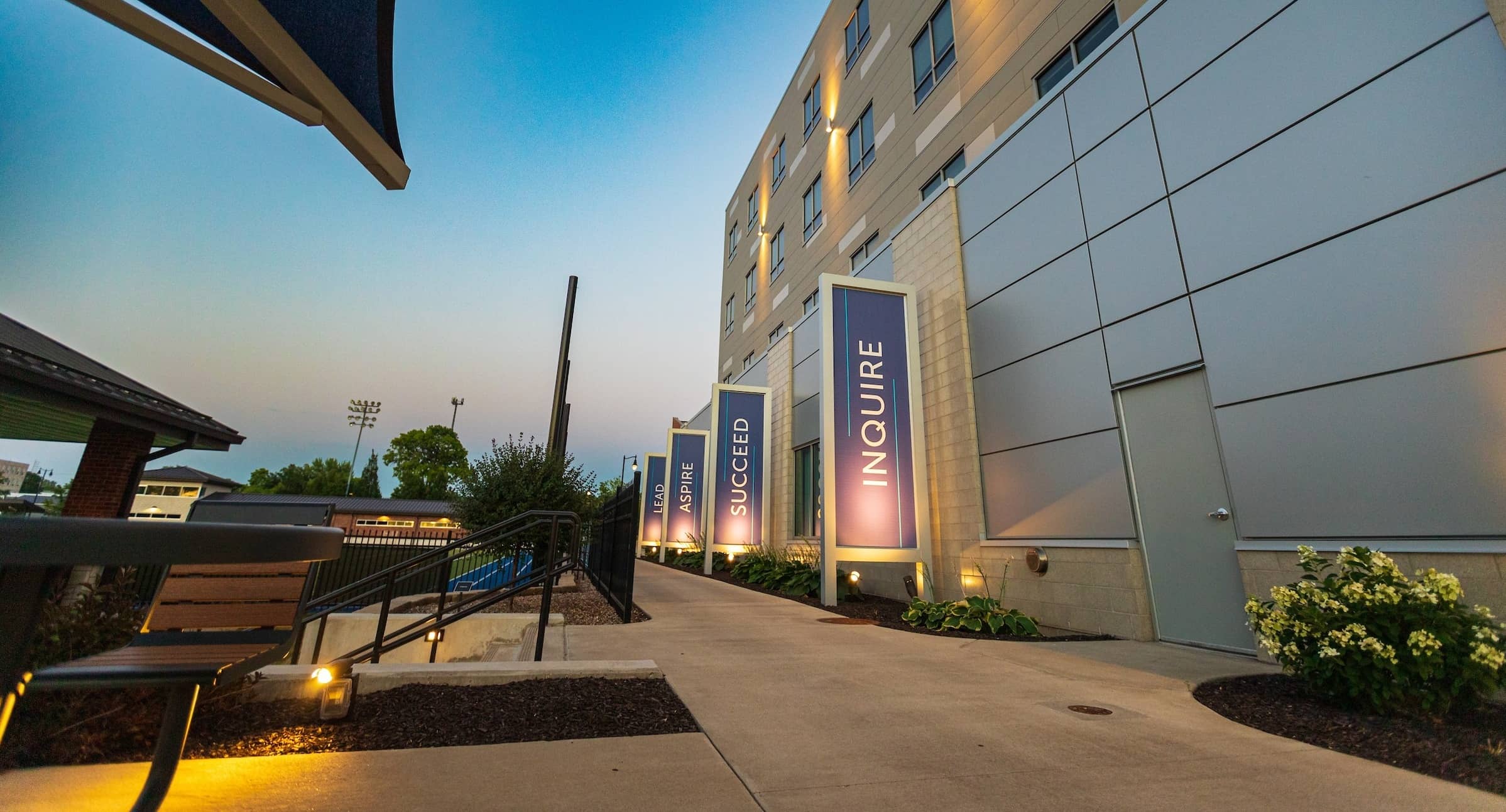 Exterior of New Hall in the evening, location for our Master of Business Analytics program, highlighting the Lead, Aspire, Succeed, and Inquire vertical signs.