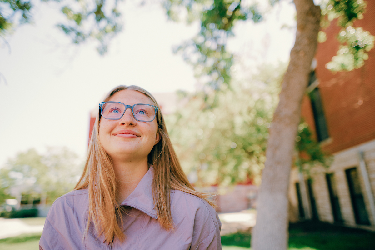 Undergraduate: Woman with long blonde hair and wearing glasses staring up at the sky.