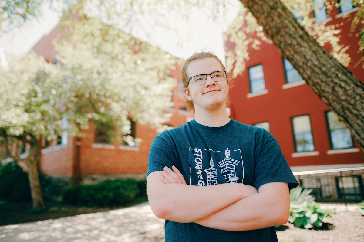 Undergraduate: Student with arms crossed wearing glasses and a Storm the Gate t-shirt.