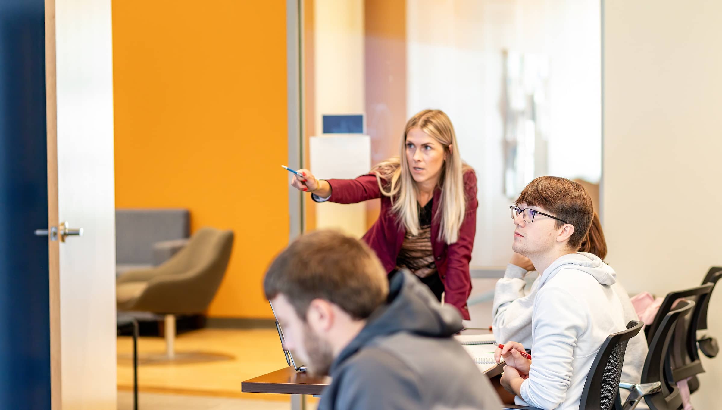 Associate Professor Gina Singleton standing in front of a table in her classroom, interacting with three Master of Accountancy (M.S.A.) program students.