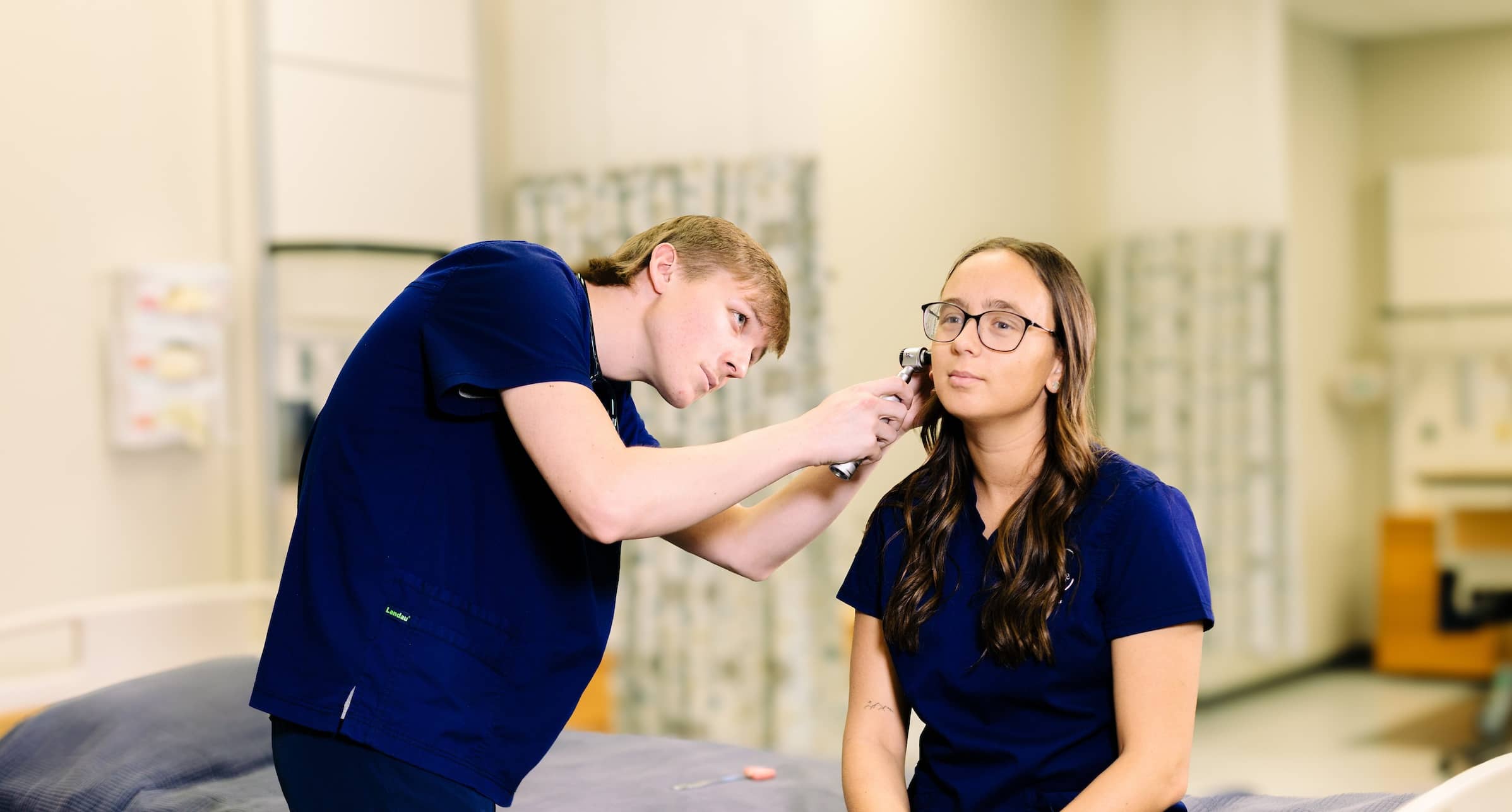 Male nursing student using an otoscope to check the right ear of a female nursing student in the (ASN) nursing associate program lab.
