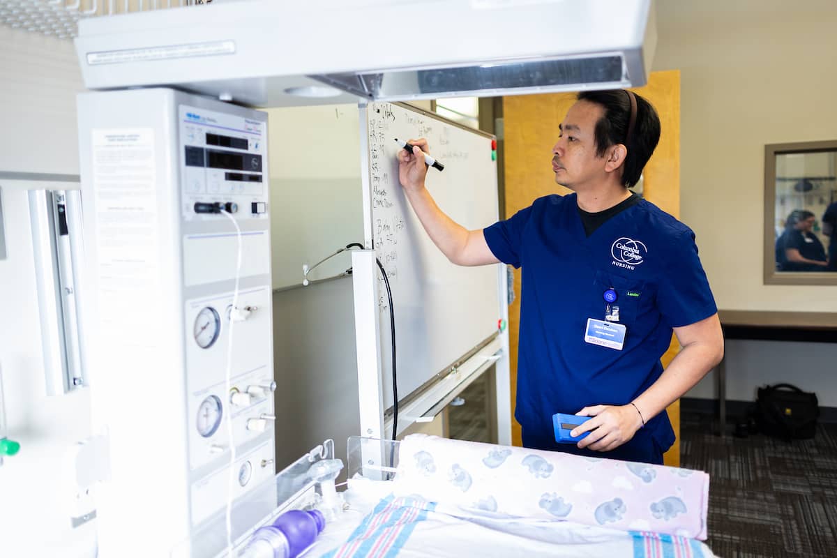 Male nursing student in the lab, writing on a marker board.
