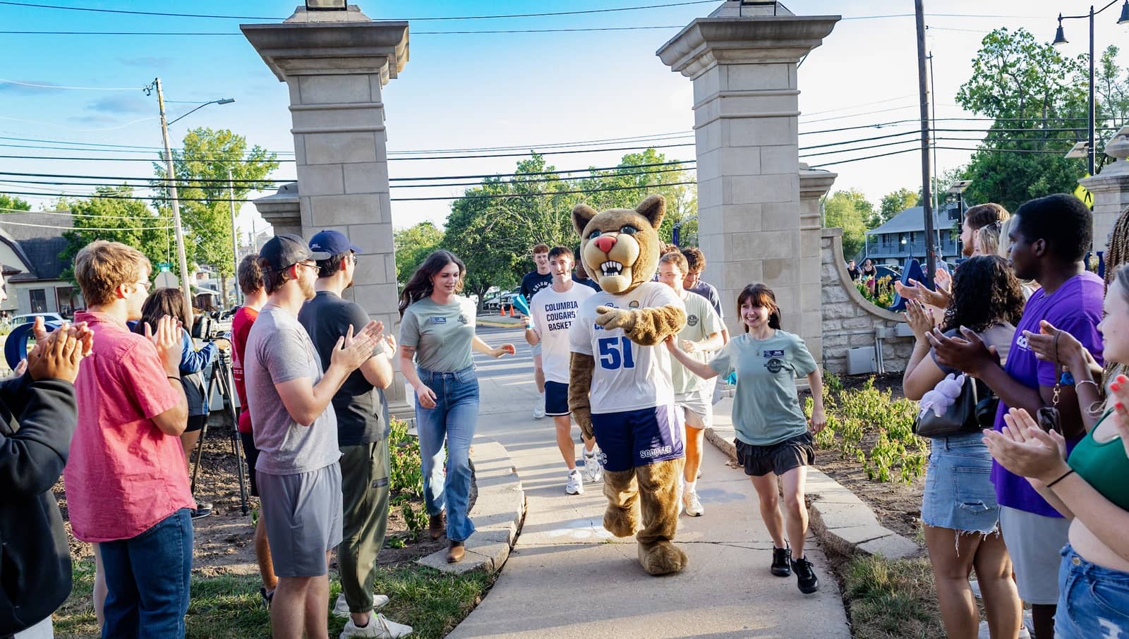 Scooter the Cougar, wearing jersey #51, leading the charge surrounded by new students through Roger's Gate for the Storm the Gate ceremony.