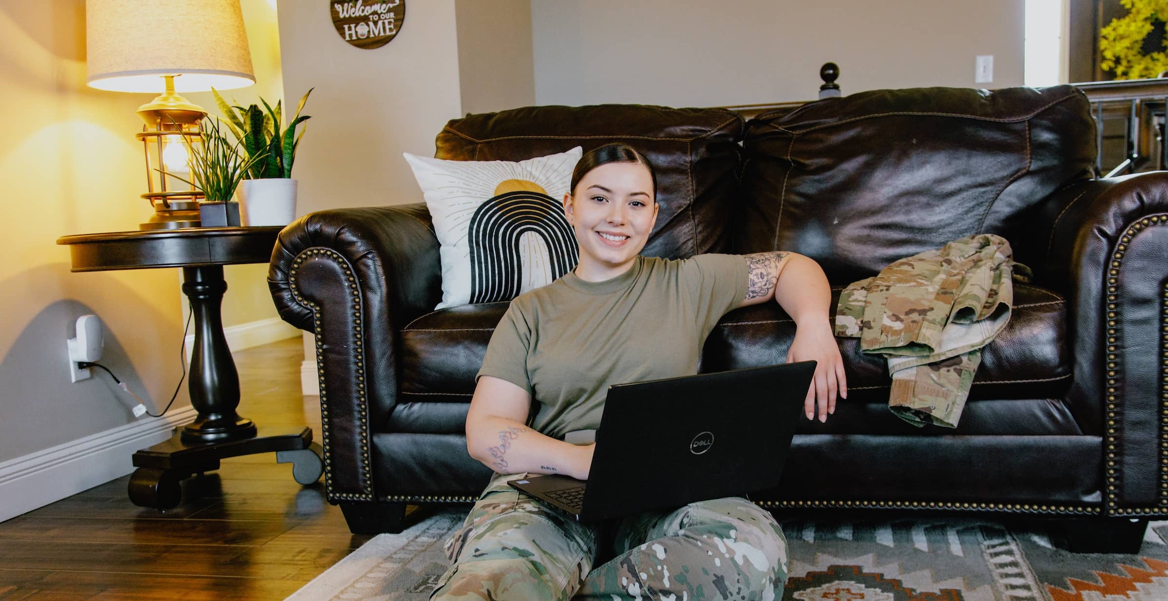 Female military member student, sitting on the floor in front of her couch with a laptop, studying for her MSW degree.