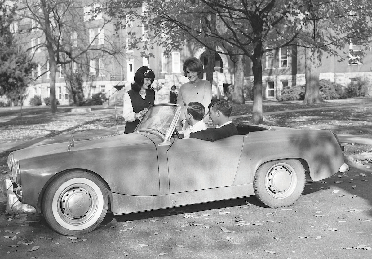 Two male students sitting in a 1960's sport convertible and two female students standing by the passengers door.