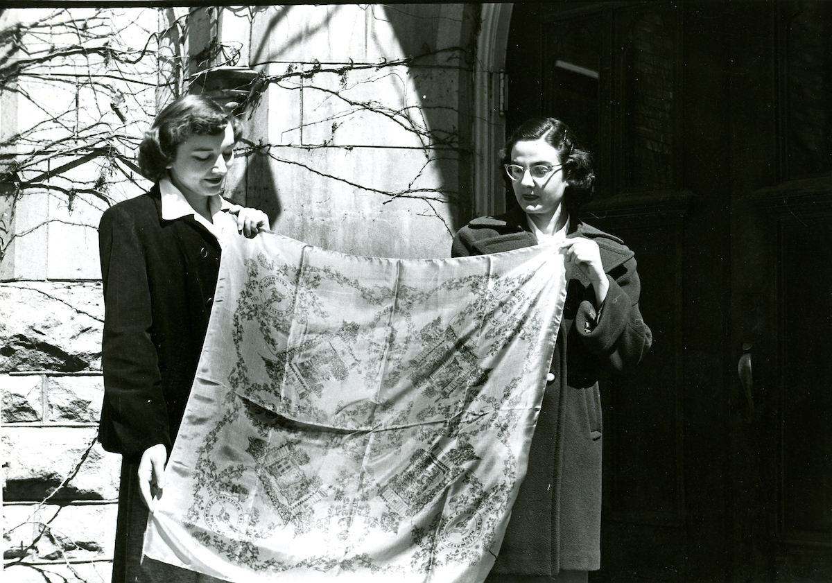 Historical image of two students holding up a decorative cloth.