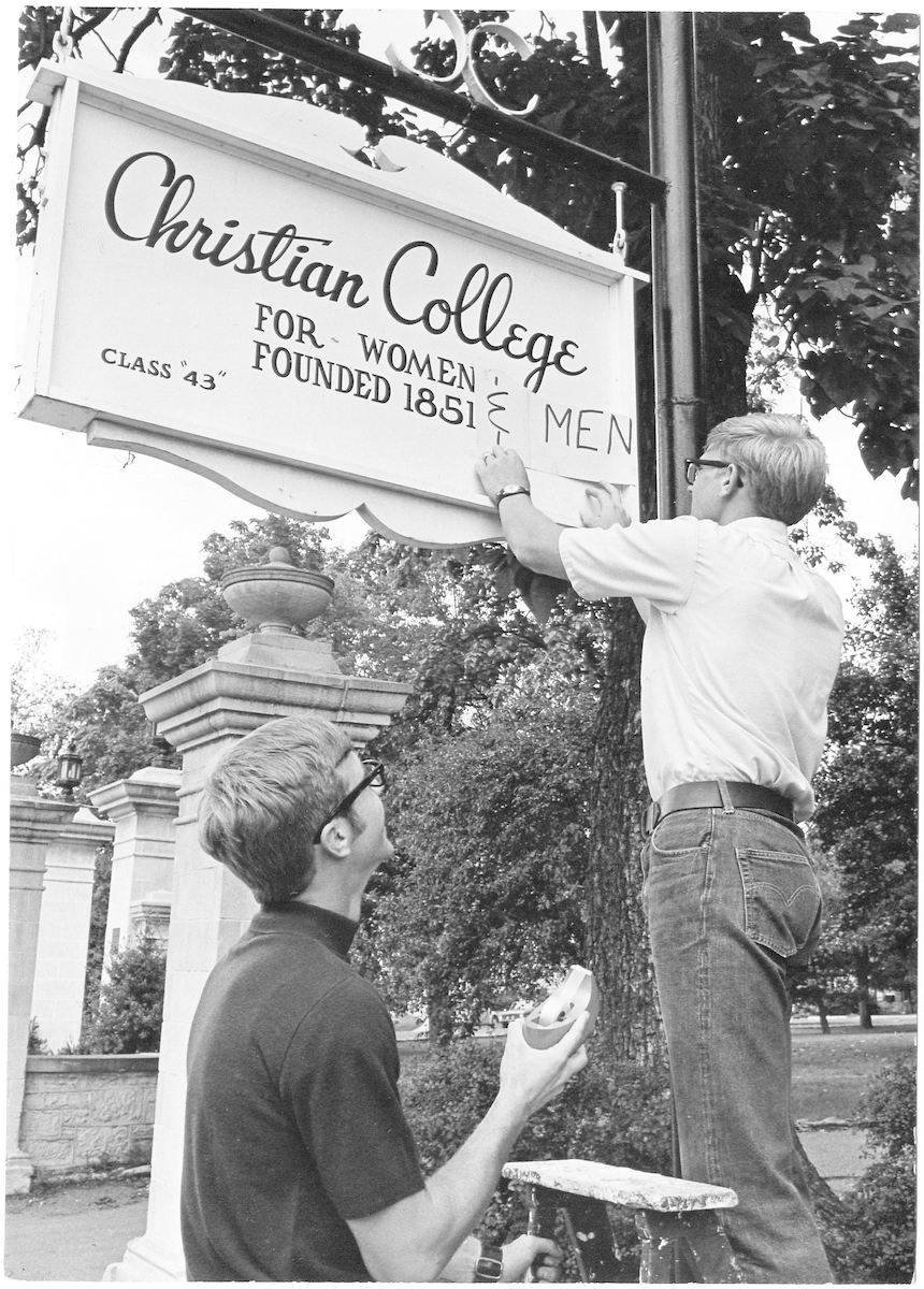 Two male students adding "For Men" to the original Christian College sign.