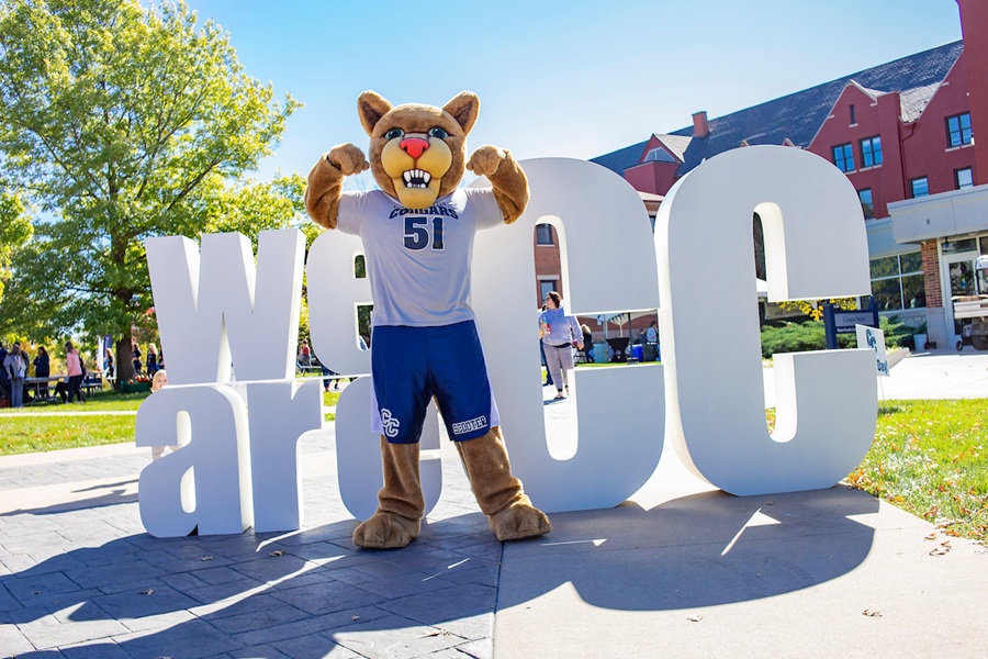 Scooter the Cougar standing in front of the We Are CC sign.
